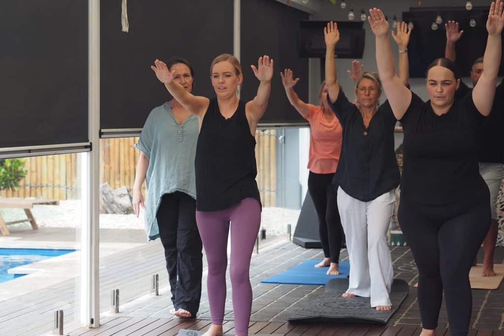 Showing group yoga participants in standing pose with raised arms