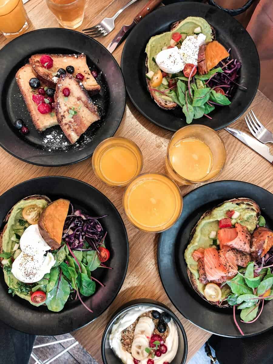 Top-down view of a vibrant brunch spread featuring avocado toast, salmon, fresh salad, and juice.