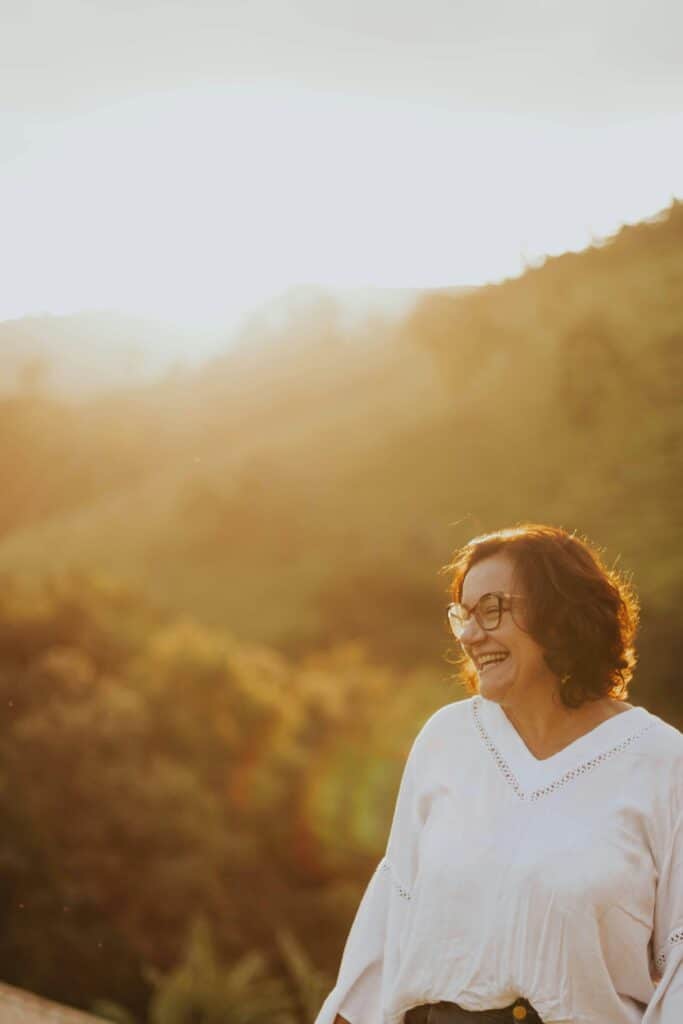 Smiling senior woman enjoying a beautiful sunset over lush countryside hills.