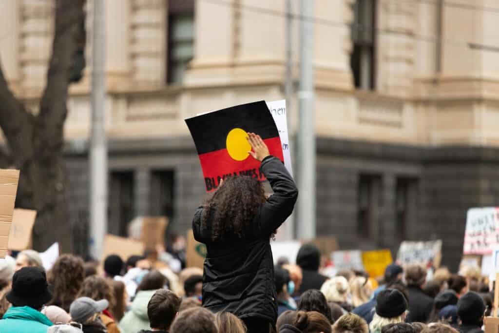 Crowd at a Melbourne protest holding signs for racial justice outdoors.