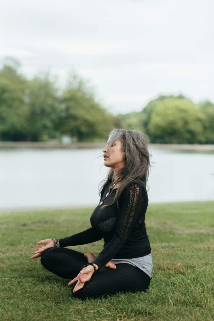 Woman meditating in lotus pose by a peaceful lakeside, embracing wellness.
